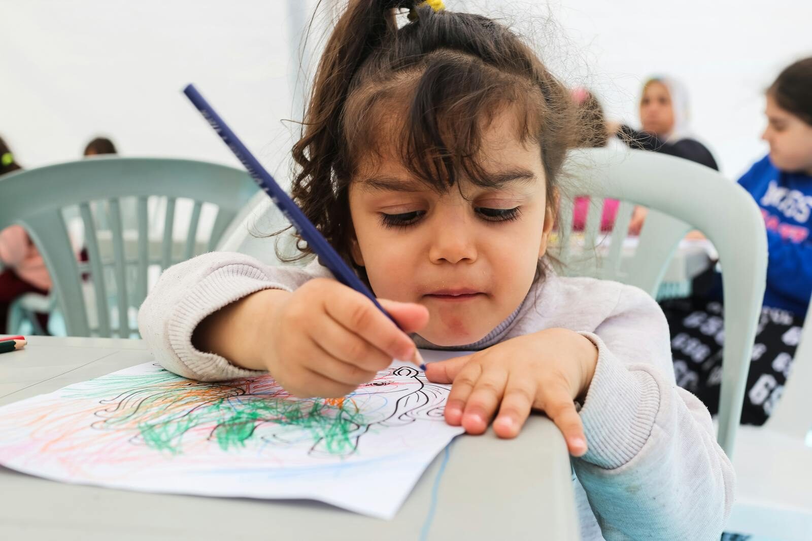 Une jeune fille absorbée par le coloriage d’une image avec des crayons dans un cadre de maternelle animé.