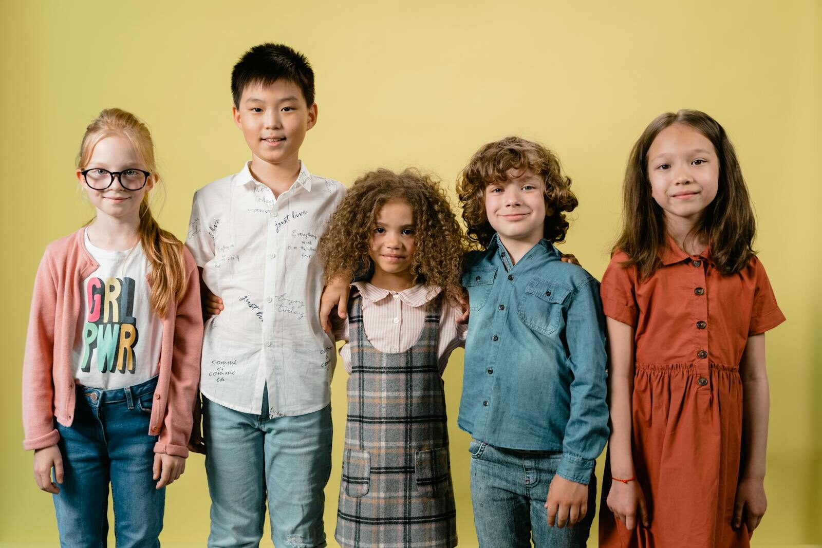 Cinq enfants divers souriant sur un fond jaune dans un cadre studio.